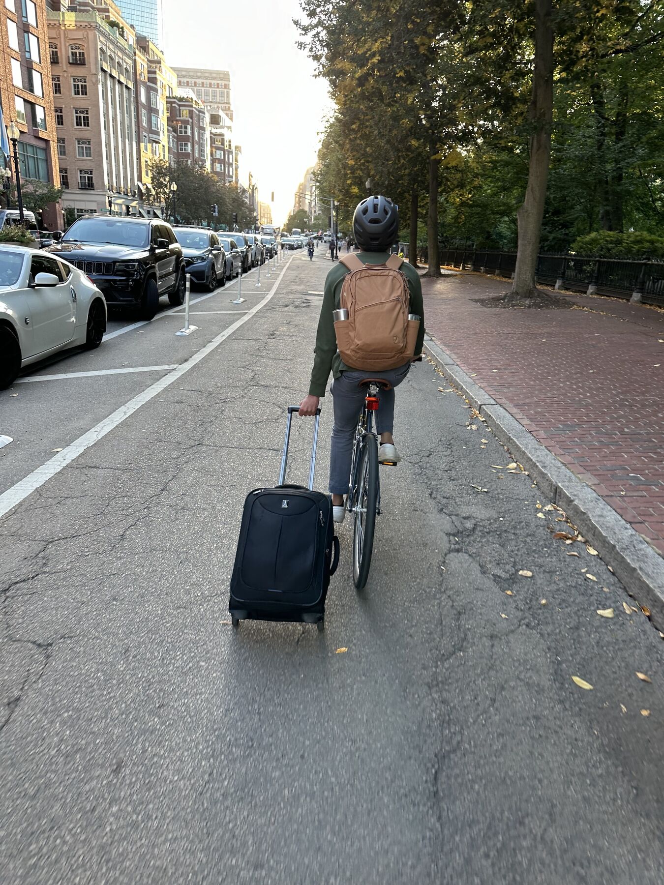 A teammate biking down a city bike lane, towing a rolling suitcase