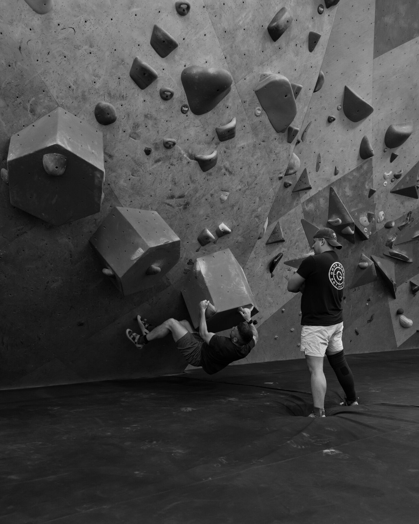 A teammate hanging from a bouldering wall while another watches