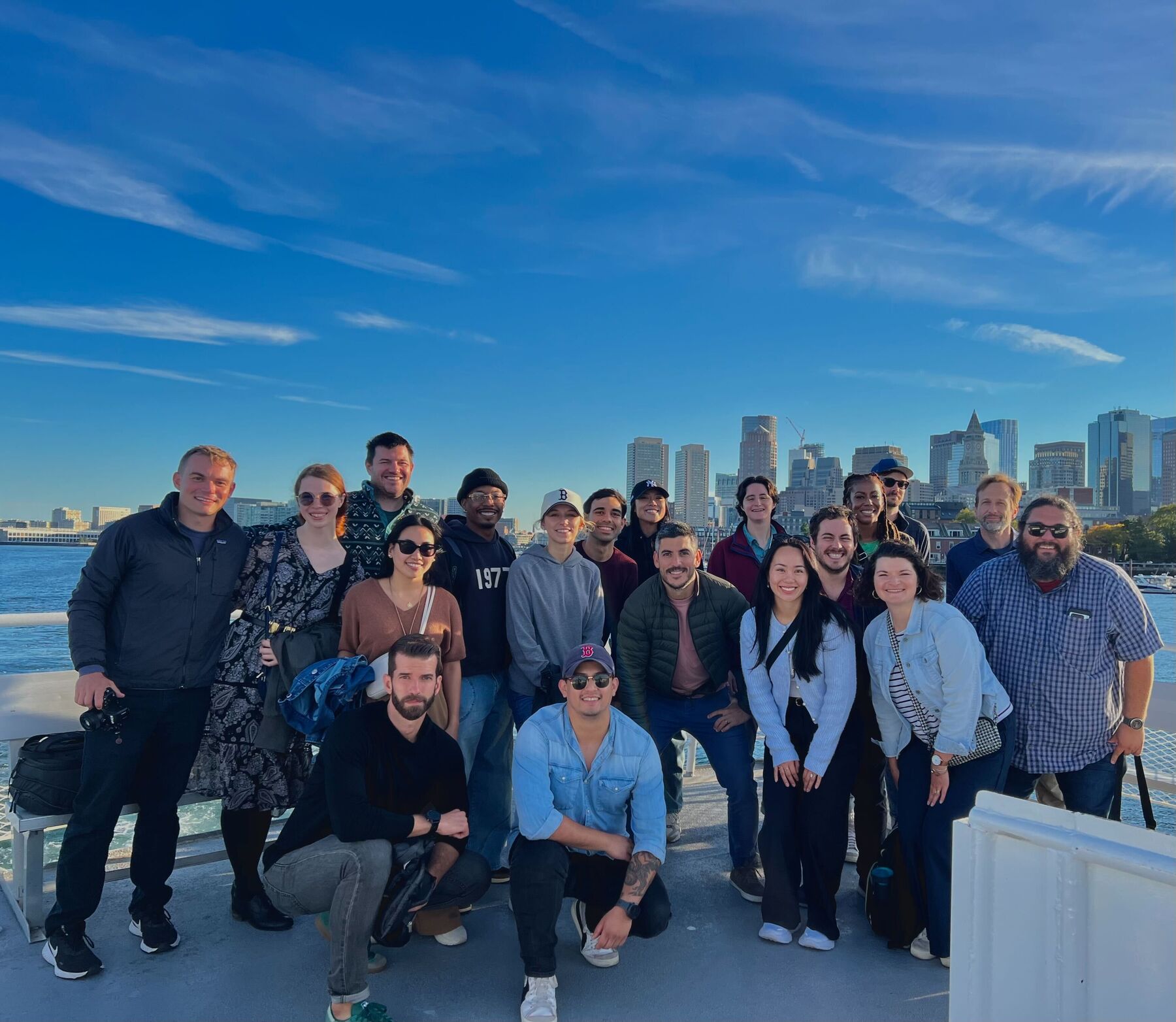 The team gathered on a boat deck with the Boston skyline behind them