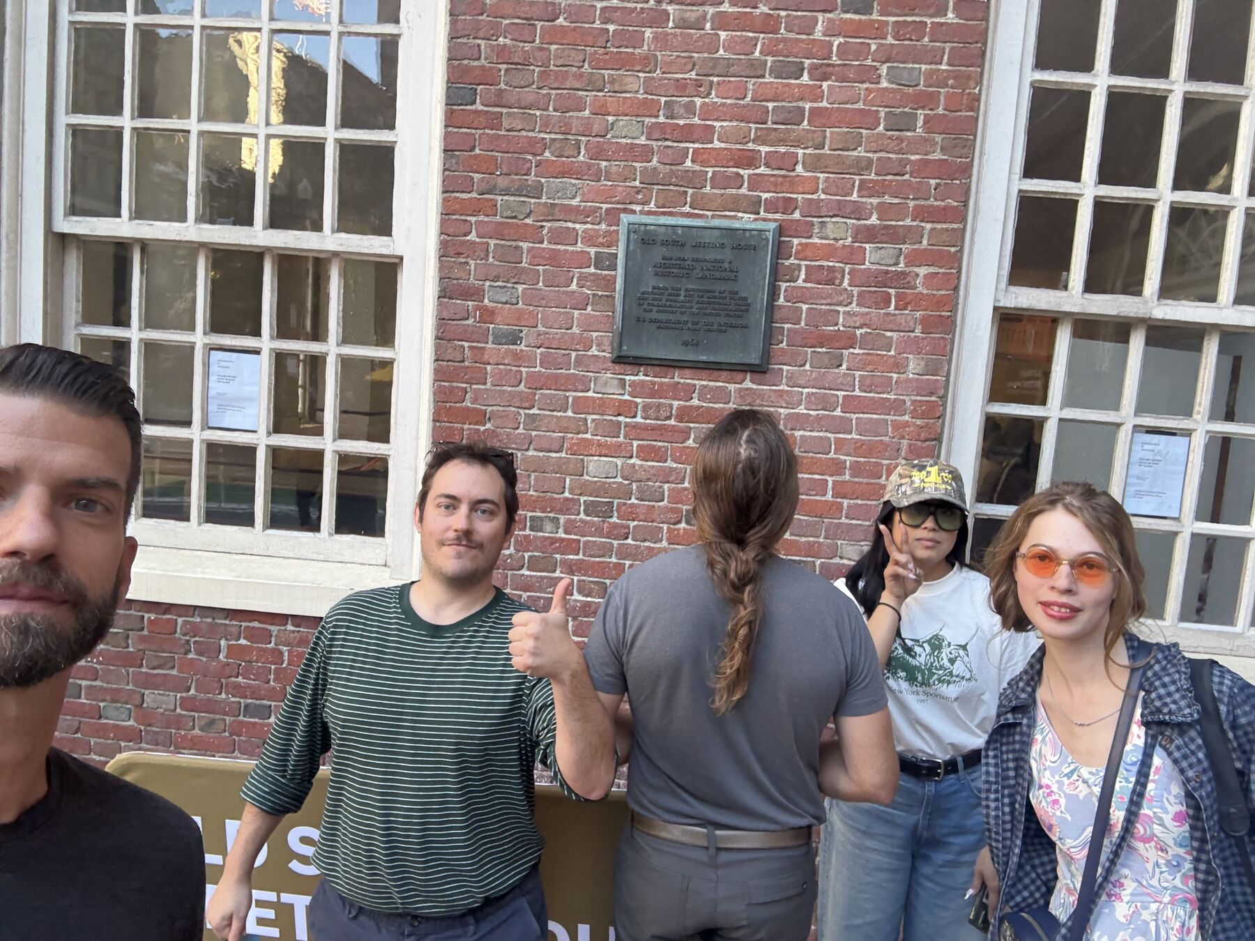 Teammates giving a thumbs-up outside a brick building